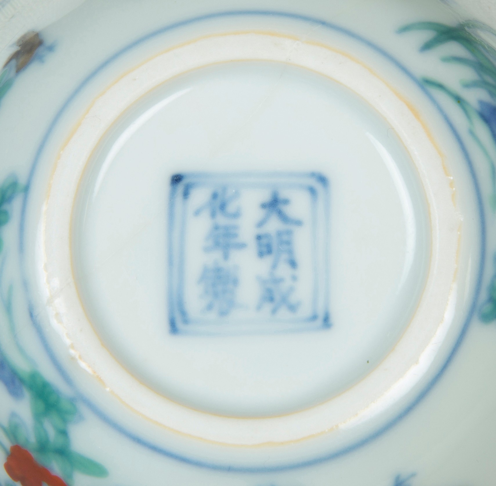 Marque de règne en caractère régulier bleu, à six caractères, enfermée dans un double cadre carré, au pied d’une porcelaine.