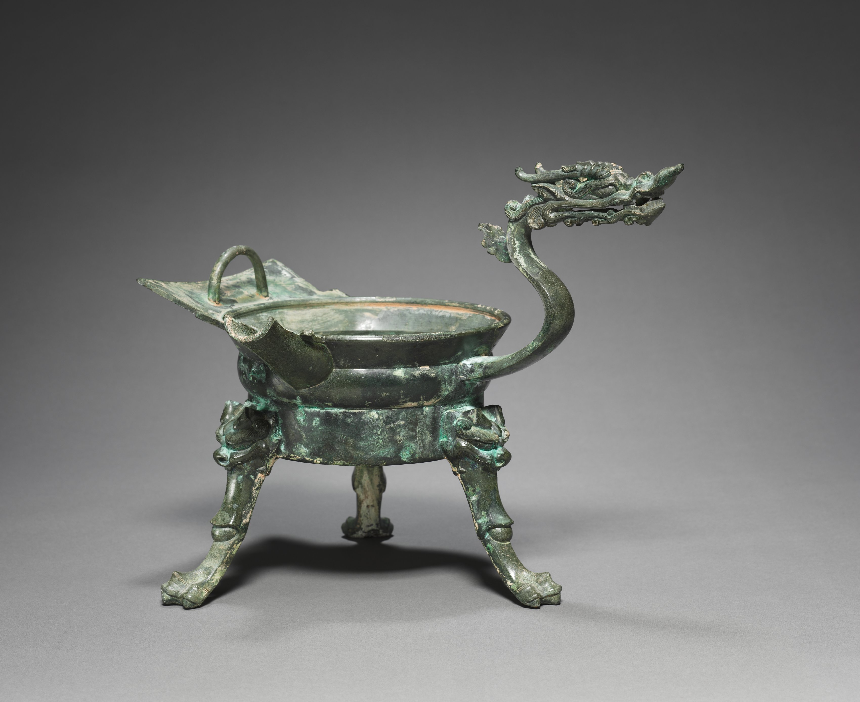 Récipient de bronze à trois pieds et anse formant une tête de dragon, patine sombre.
